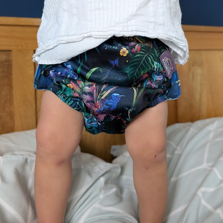 Person wearing colorful floral-patterned cloth nappy sitting on a bed.