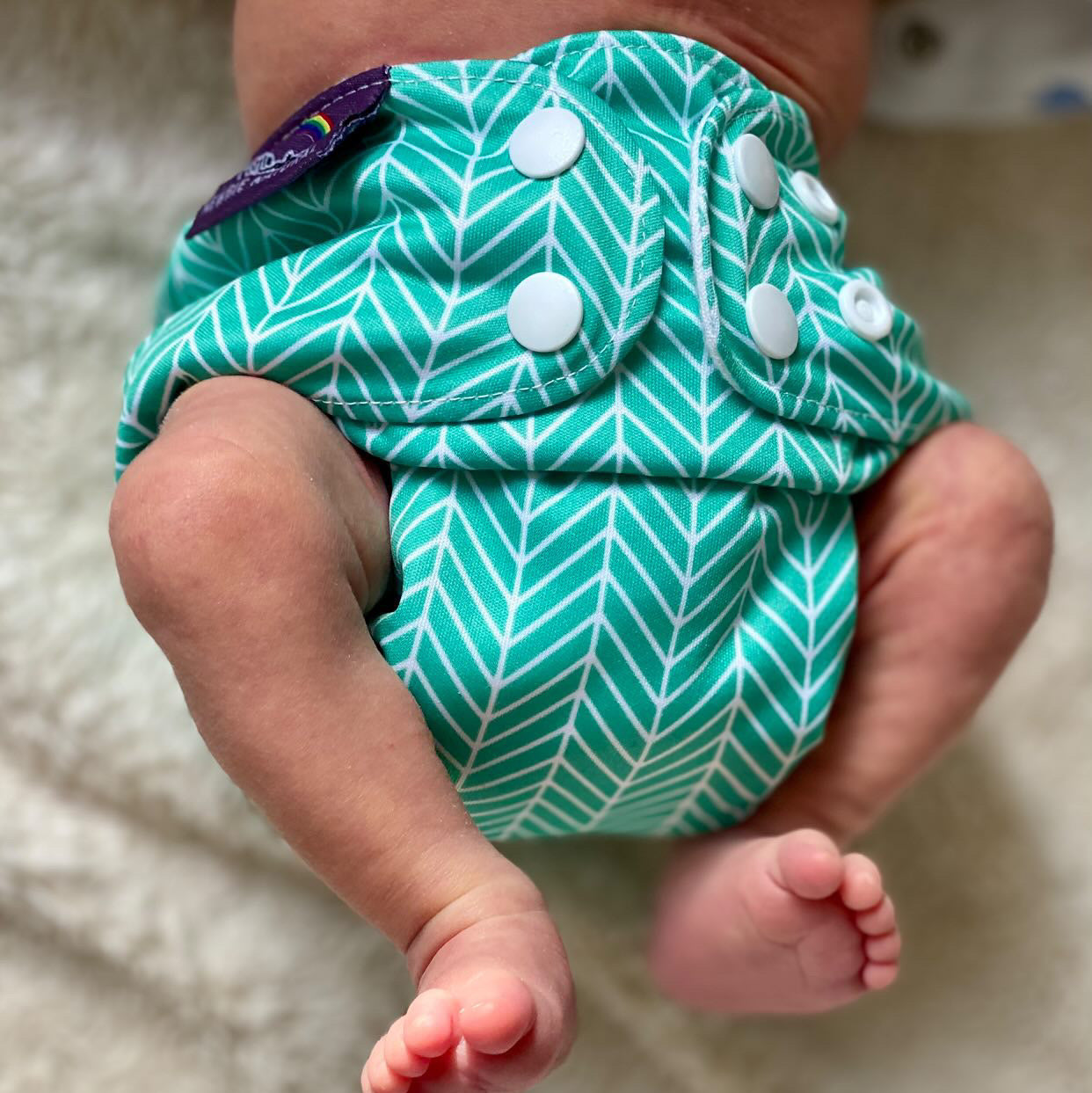Baby wearing a green and white patterned diaper on a neutral background