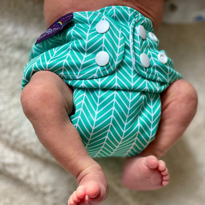 Baby wearing a green and white patterned diaper on a neutral background