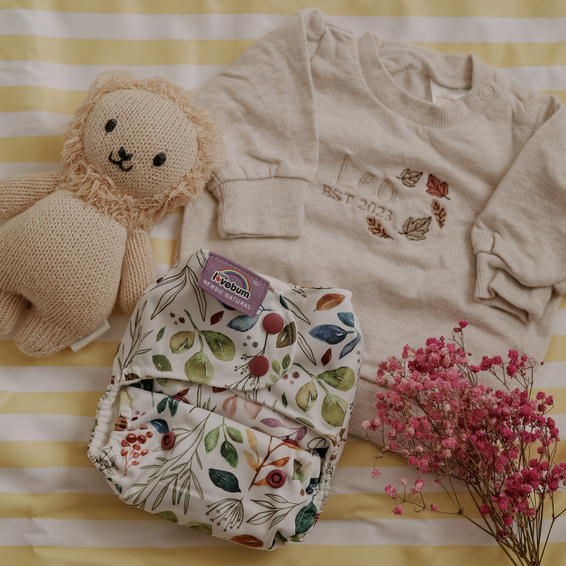 Baby clothing and toy on a striped yellow and white background