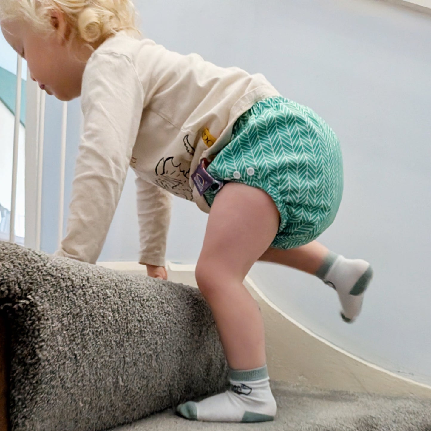 Child wearing a green patterned diaper standing on a staircase.