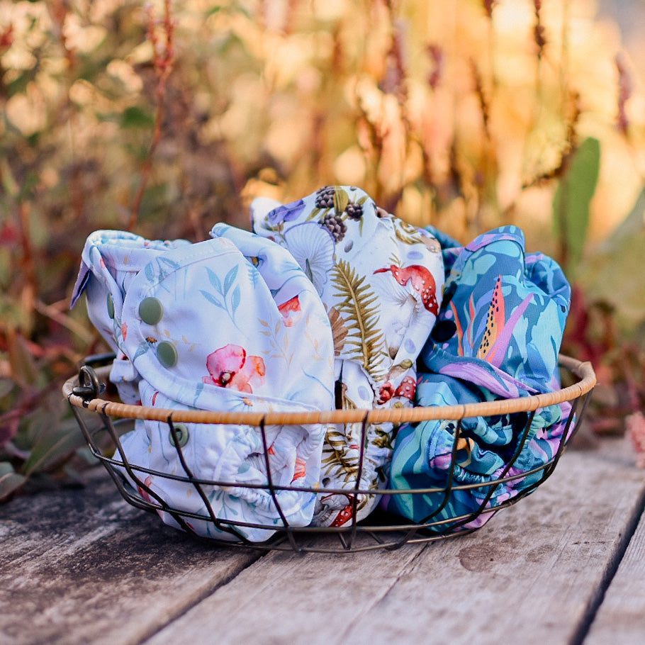 3 newborn nappy covers in a basket outdoors
